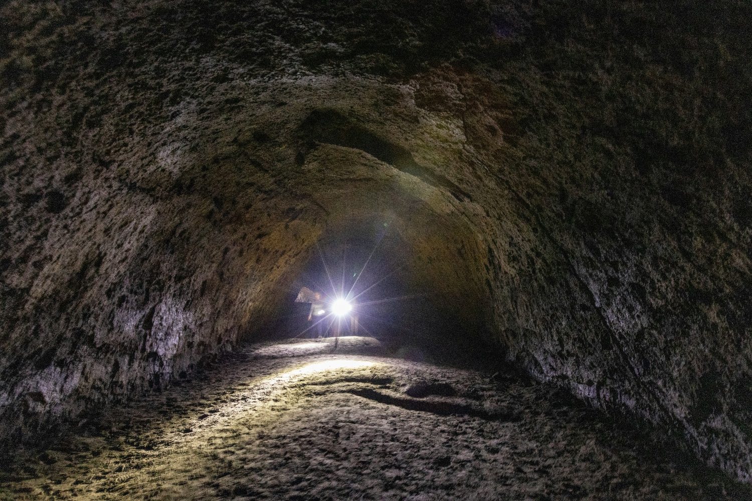 Explorer standing inside a dark tunnel with a bright flashlight.